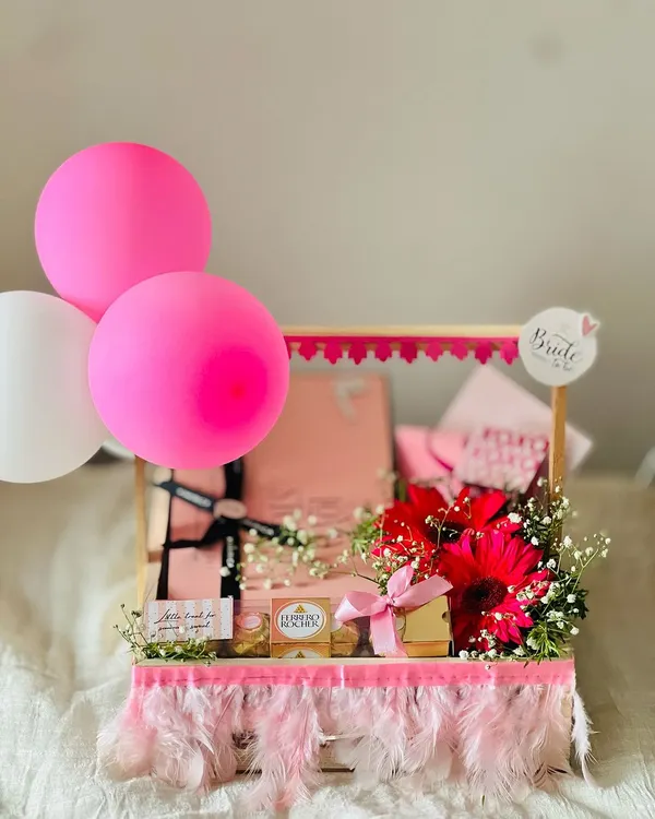 A vibrant and celebratory 'Bride to be' hamper, perfect for a bachelorette party or bridal shower. It's decorated with pink feathers, balloons, and fresh flowers for a fun, festive look.