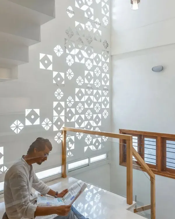 The play of light and shadow through a custom-designed jali screen creates a dynamic, shifting pattern on the wall of this staircase, turning a simple surface into a piece of art.