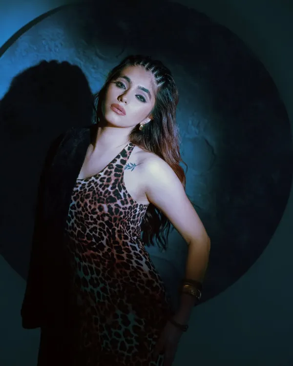 A moody shot from a fashion editorial, using a single spotlight against a dark background. This dramatic lighting creates a cinematic feel, perfect for showcasing the bold leopard print dress.