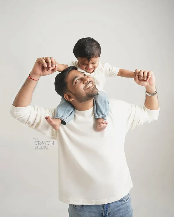 The view from dad's shoulders is always the best. This studio portrait captures the pure joy and laughter between a father and son, set against a simple white background to let their connection shine.