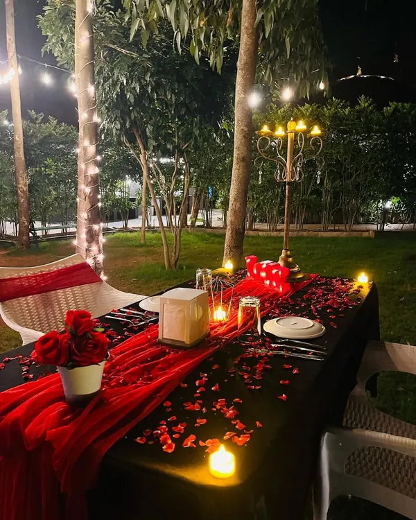 An example of a romantic outdoor dinner for two. I handle the complete table arrangement, including a table runner, scattered rose petals, a candelabra centerpiece, and ambient lighting from LED candles and overhead string lights for a private, cozy atmosphere.