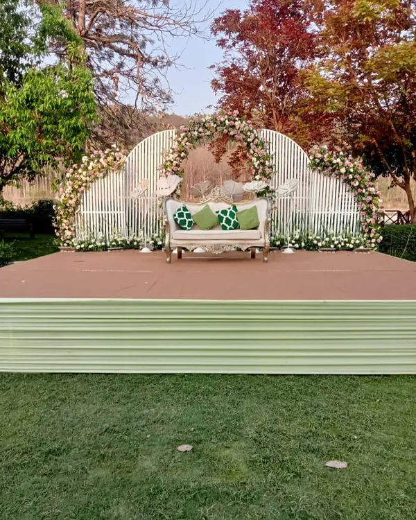 A beautiful day wedding stage with a modern white slatted backdrop, adorned with white and green floral arrangements. The vintage sofa adds a touch of classic elegance.