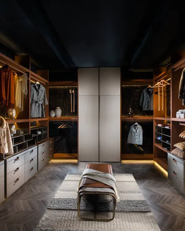 A luxurious walk-in wardrobe designed as a complete dressing room. It combines open shelves for display, deep drawers for organization, and a central bench, all brought together with warm colors and plush textures for a contemporary yet comfortable setting.