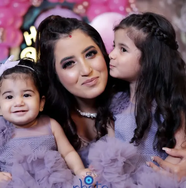 A mother and her two daughters, with the older sister giving her mom a sweet kiss on the cheek. This candid moment was captured during a first birthday party with a Barbie theme.