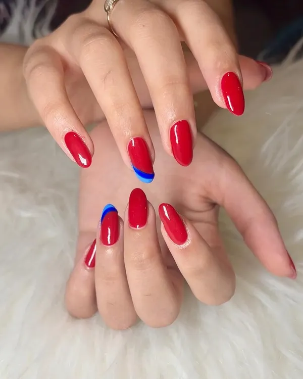 A classic red manicure with a twist. This set features glossy, almond-shaped red nails with a surprise abstract swipe of bright blue on two accent nails.