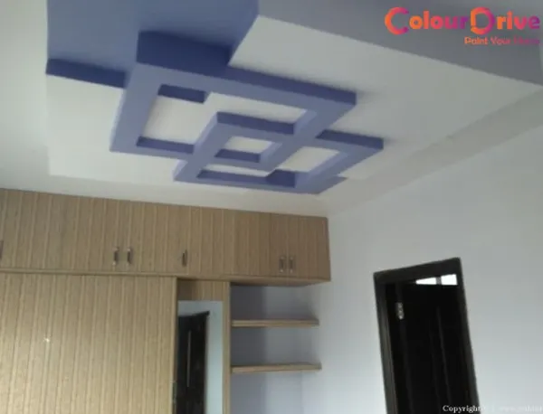 A bold, interlocking geometric false ceiling design in a two-tone color scheme. This POP construction adds a strong visual focus to the bedroom and complements the existing wooden wardrobes.