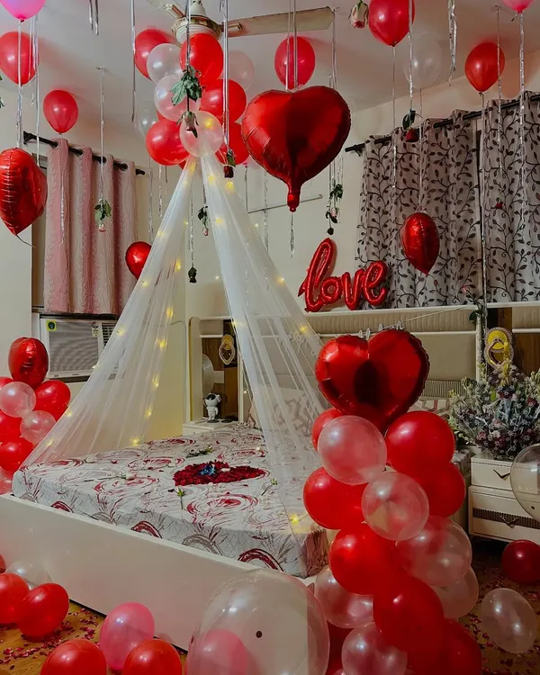 A complete romantic room decoration for a birthday or anniversary surprise. I used a canopy with fairy lights over the bed, red heart-shaped balloons, and loose balloons on the ceiling and floor.