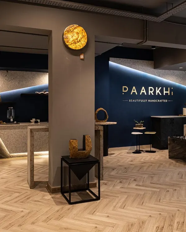 An overall view of the Paarkhi boutique, showing how the reception area and bar section were designed to mirror each other. The signature 'Paarkhi blue' wall with gold branding serves as a powerful anchor for the entire space.