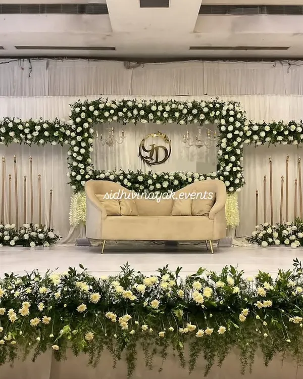 A classic and elegant engagement stage. This setup features a beautiful frame of white flowers and greenery, with sophisticated seating, perfect for timeless photos.