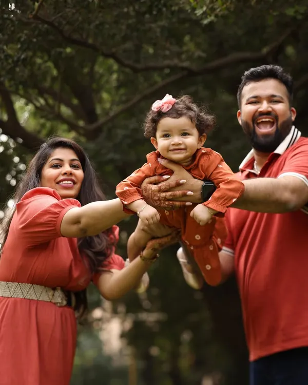 Pure, unadulterated joy. This family portrait in a beautiful garden setting captures a moment of fun and flight, with the parents lifting their little girl up in laughter.