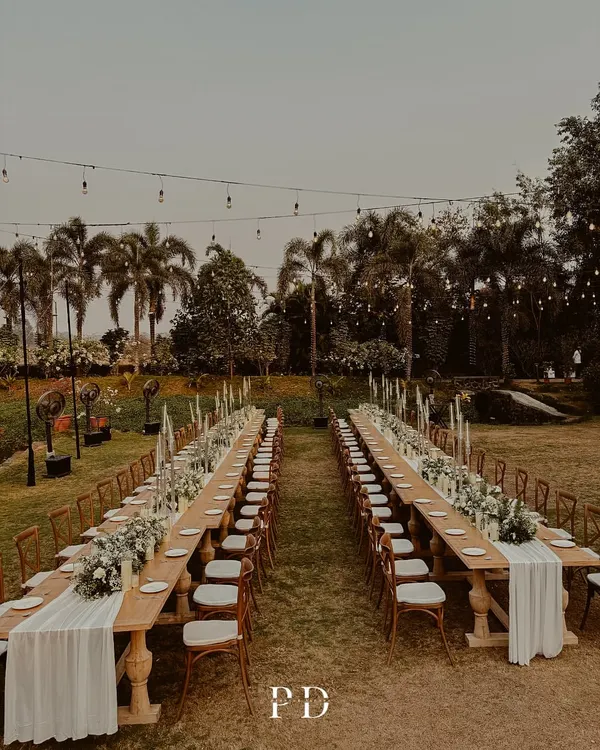 A breathtaking view of our long-table sit-down dinner setup. The combination of rustic wooden tables, a full floral runner, and a canopy of fairy lights creates an atmosphere of pure enchantment.