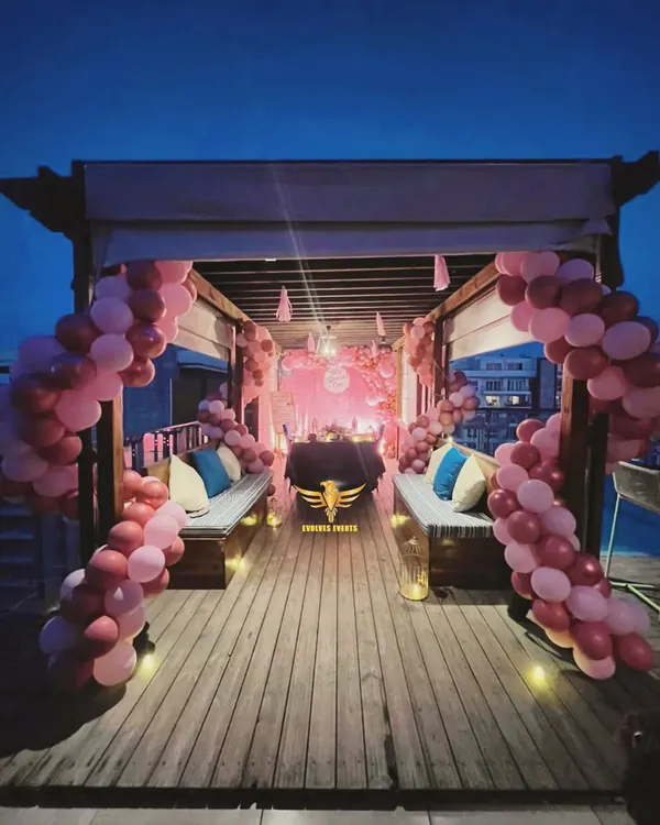 A beautiful rooftop candlelight dinner setup. The decor features a cabana draped with pink balloon arches, creating a private and romantic dining experience under the stars.