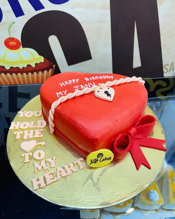A beautifully crafted heart-shaped fondant cake in vibrant red, perfect for a birthday or anniversary. The design features a rope detail and a small lock, symbolizing a special bond.