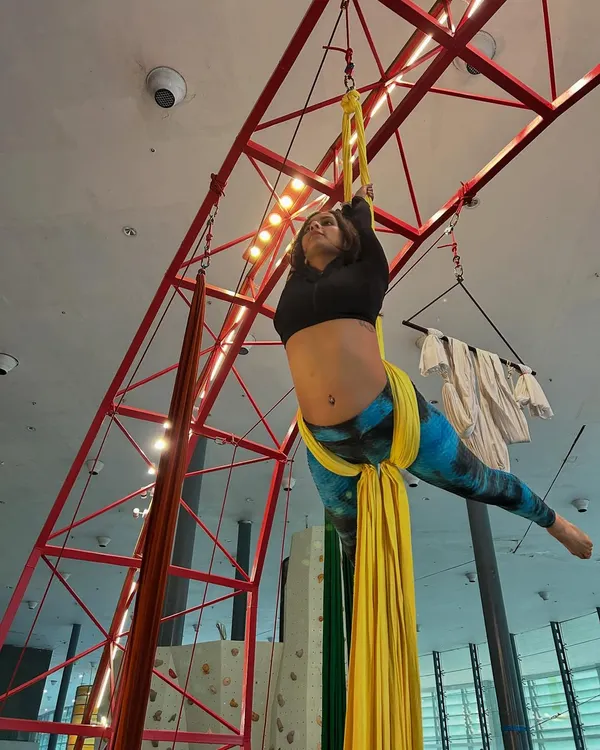 An aerialist hangs suspended from yellow silks, demonstrating the core strength and balance central to our silks classes.
