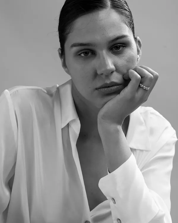A raw and intimate black and white portrait. The minimal styling and close framing create a powerful sense of connection, focusing entirely on the subject's contemplative expression.