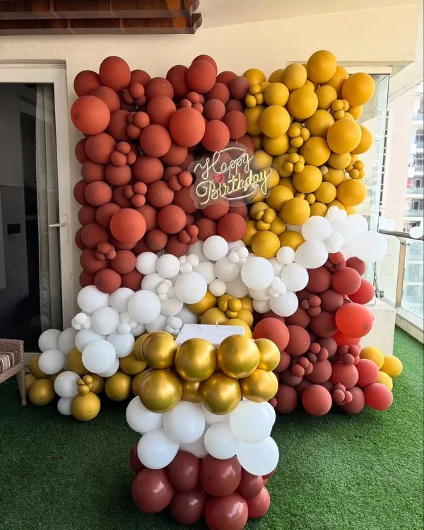 A full balloon wall in rustic shades of brown, gold, and white, complete with a pedestal for a cake. This makes for a stunning and unique photo backdrop.