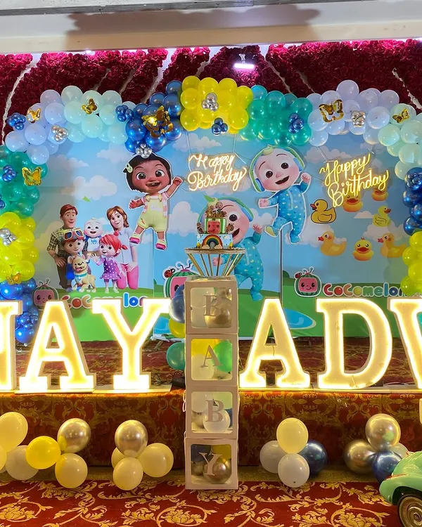 A colorful Cocomelon birthday party featuring a full balloon arch, a themed backdrop with all the characters, and large, light-up letters spelling out the birthday boy's name.