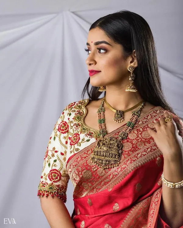 A stunning bridal portrait in a vibrant red saree, showcasing antique temple jewelry and an intricately embroidered blouse. A perfect blend of tradition and elegance.