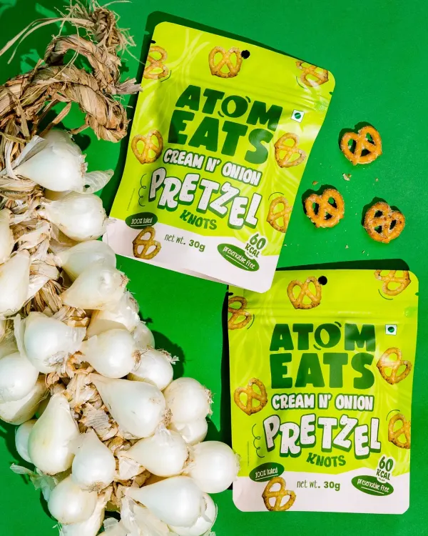 A vibrant flatlay for cream and onion pretzel knots, styled with fresh pearl onions against a bold green background. This composition connects the product to its core ingredient in a fun, graphic way.