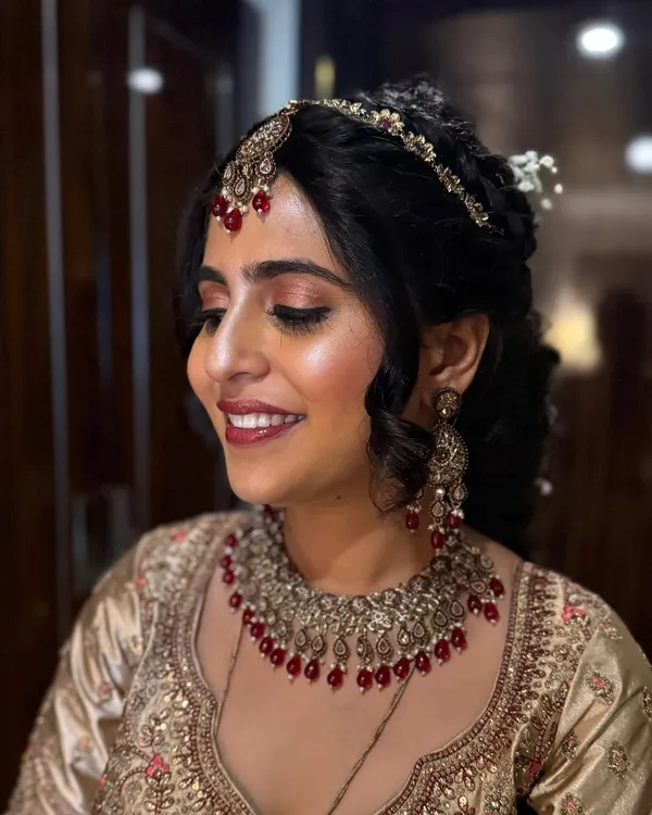 A glowing bride ready for her wedding ceremony. Her look features a soft, romantic updo with intricate braids and a traditional matha patti, paired with radiant makeup that enhances her natural features.