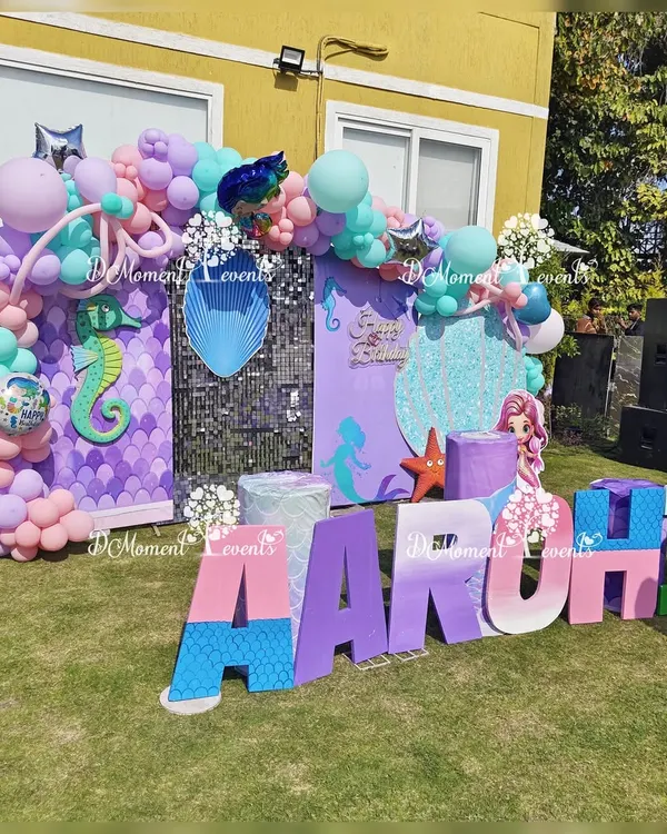 An amazing outdoor mermaid-themed stage, complete with a sequin wall, custom marquee letters, and props of various sea creatures, all set up on a sunny lawn.