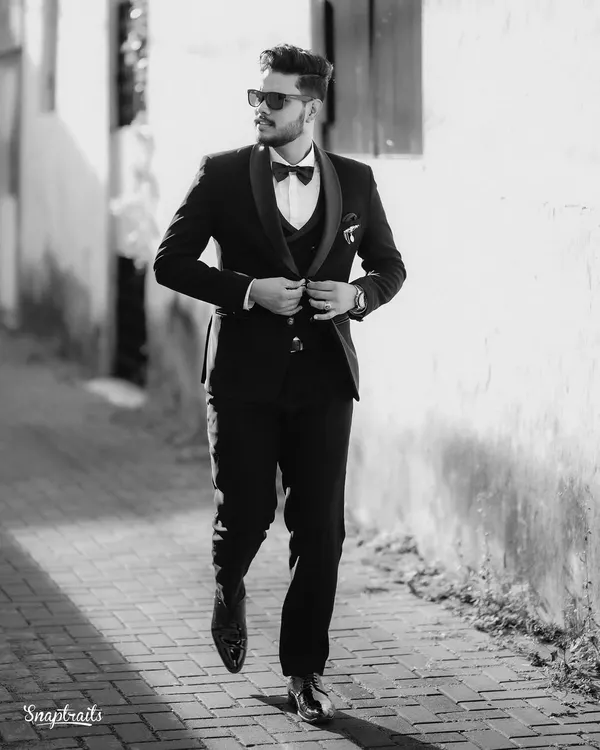 A classic black and white shot of the groom, looking sharp and confident in his tuxedo as he walks down a sunlit alley.