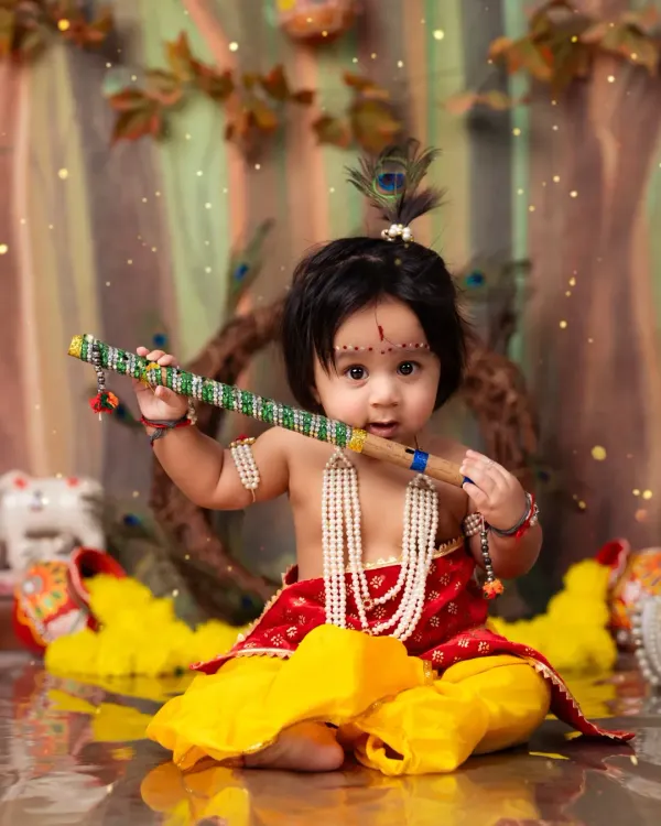 A playful little Krishna, sitting up and holding his flute in a whimsical forest setting.