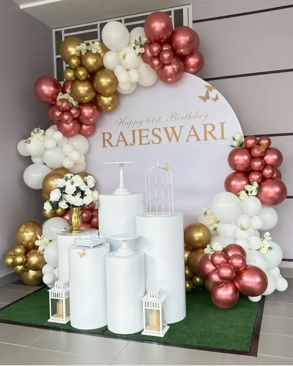 An elegant 61st birthday for Rajeswari with a personalized round backdrop. The decor features a sophisticated color palette of rose gold, white, and gold, with clean white plinths and lanterns.