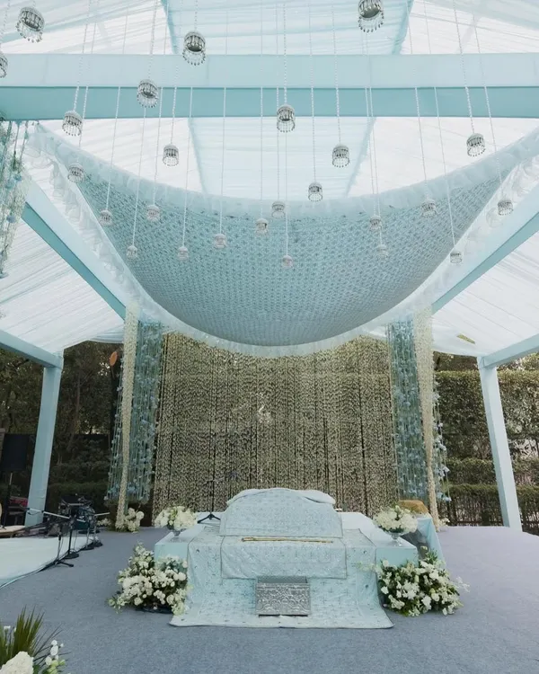 A serene and elegant setup for an Anand Karaj ceremony. The design features a soft powder blue and white color palette, with a stunning ceiling installation of cascading white flowers creating a divine canopy.