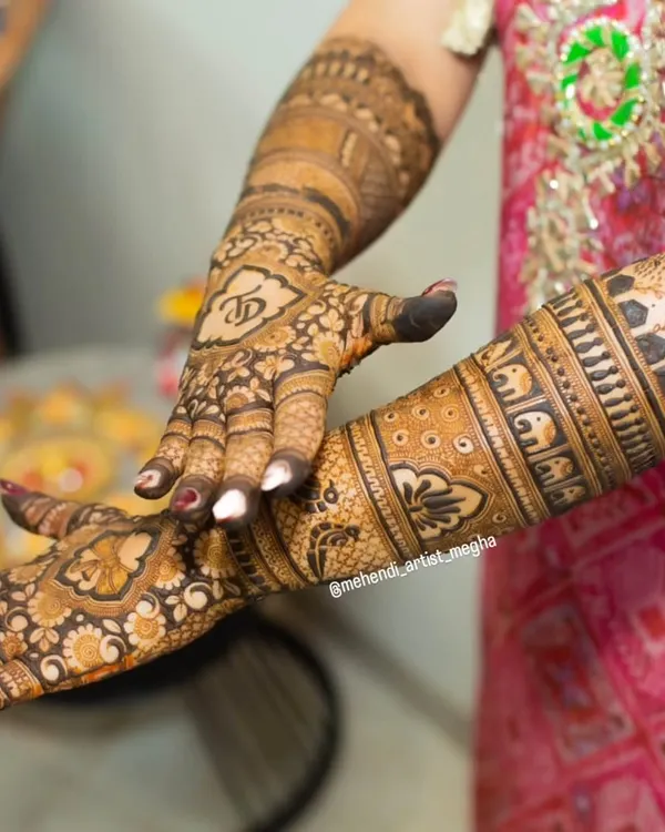A close-up showing the bride's initial 'V' beautifully integrated into the intricate design on the back of her hand. This is a wonderful way to personalize your mehendi.