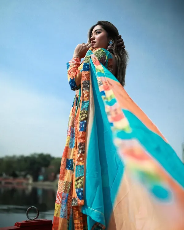 A beautiful shot of a model in a multi-colored Anarkali, with her dupatta flowing in the wind on a boat at Yamuna Ghat.