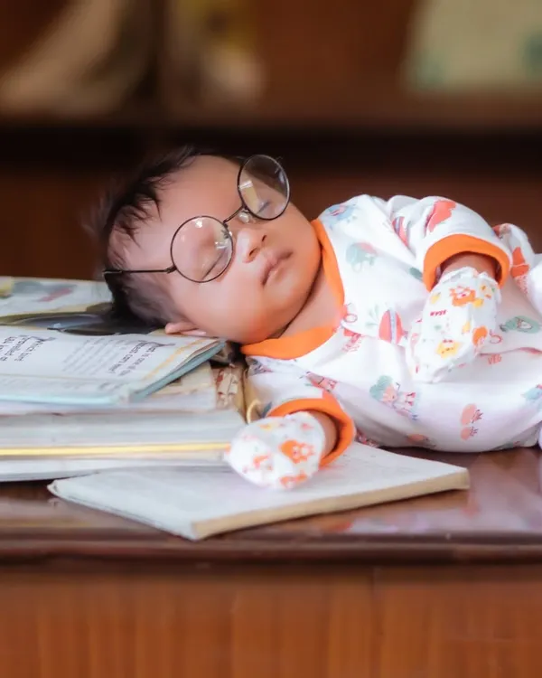 A sleepy little scholar. This creative newborn setup features a baby peacefully napping on a stack of books, complete with adorable oversized glasses.