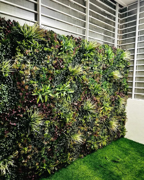 A close-up of one of our premium vertical garden walls. We use a variety of artificial plants with different textures, shapes, and shades of green and purple to create a dense, realistic, and visually interesting surface.