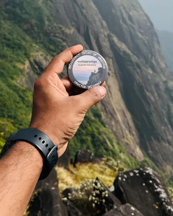 The Kumara Parvatha trek badge held against the dramatic sheer cliffs of the mountain. This trek is not for the faint of heart, but the views are epic.