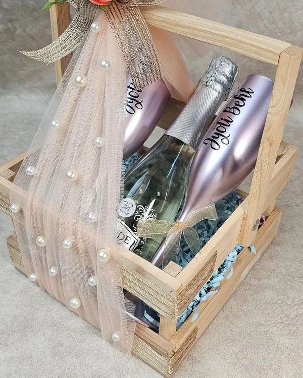 Here's to celebrating love that lasts. This anniversary hamper, featuring personalized champagne glasses and a bottle of bubbly, is nestled in a rustic wooden basket and finished with delicate florals and netting. It’s a perfect toast to another year of shared memories.