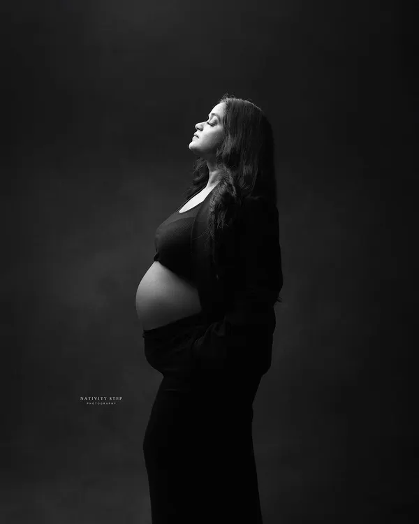 A powerful and classic black and white profile shot. The lighting beautifully sculpts the baby bump, creating a strong and timeless image of motherhood.