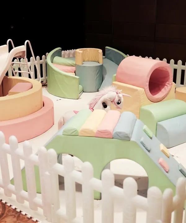 A dedicated soft play area for toddlers, set up with a ball pit, slide, and cushioned climbing structures, all enclosed by a white picket fence for safety.