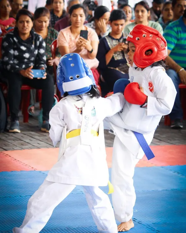 Two of our young female students engage in a controlled kumite (sparring) match during a championship. Dressed in full protective gear, including head guards and gloves, they demonstrate proper technique and sportsmanship, highlighting our focus on safe and practical self-defense training for girls and boys.