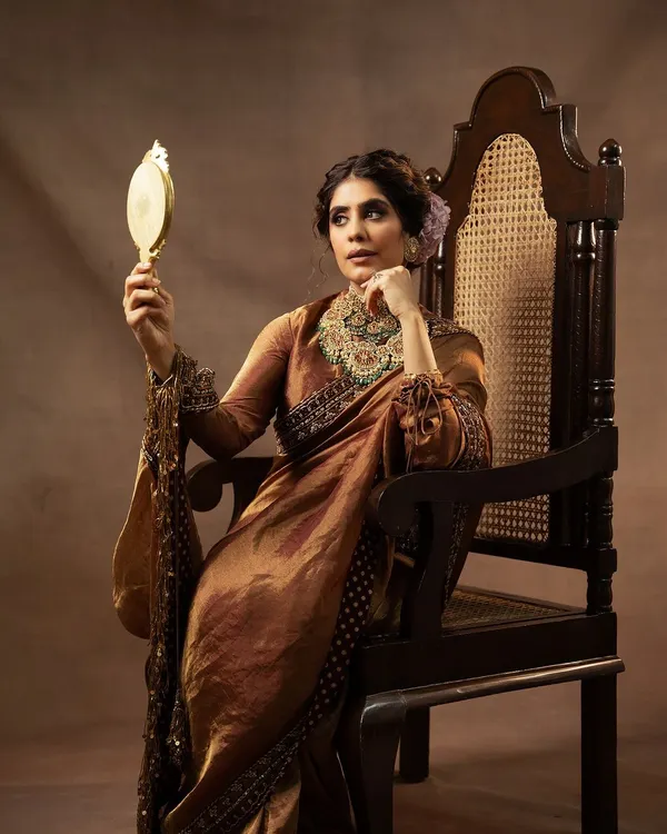 A regal portrait for Indian Couture Week, capturing the essence of heritage and luxury. The model is seated on a throne-like chair, adorned in a Divani India saree and exquisite Kishandas jewellery, creating a timeless and majestic image.