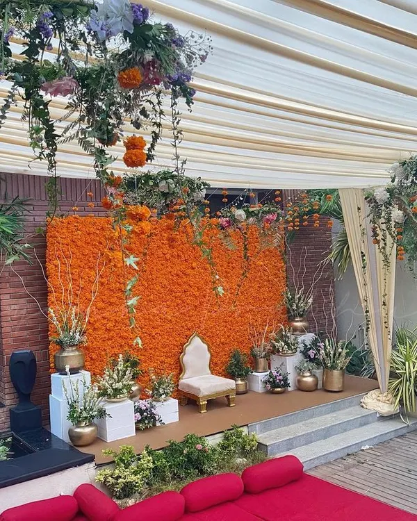 An outdoor Haldi ceremony setup featuring my signature dense marigold wall. The stage is complemented by a floral chandelier and comfortable floor seating, creating a festive and inviting space for guests.