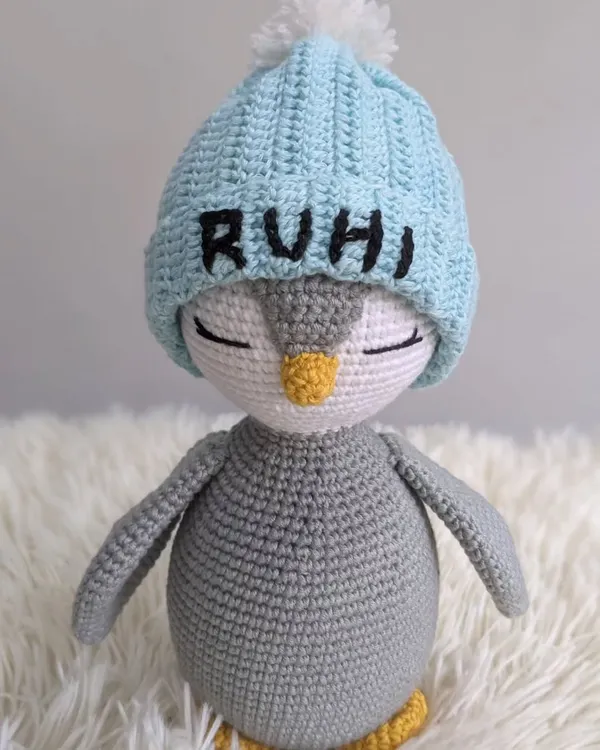A sleepy little penguin, handmade with love. This one wears a custom light blue beanie with the name 'RUHI' embroidered on it, making it a truly personal amigurumi keepsake.