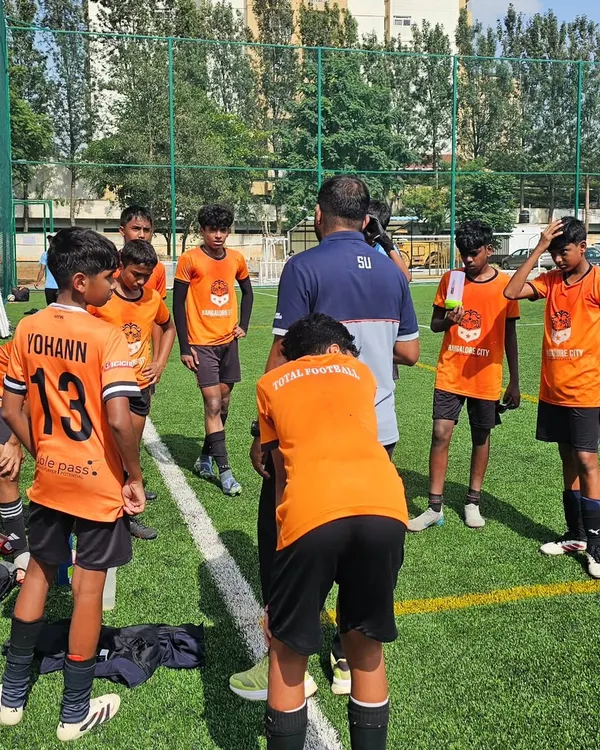 Tactics, teamwork, and our Total Football philosophy in action. A coach briefs the team during a water break, ensuring every player understands their role on the pitch.