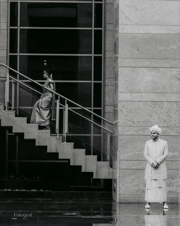 An artistic, black and white shot that plays with architecture and perspective. The groom waits as his bride descends, a moment of anticipation frozen in time.