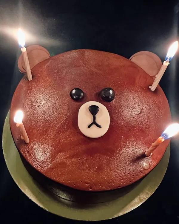 A simple and adorable bear face cake, perfect for any celebration. The lit candles show it's ready for a birthday wish.