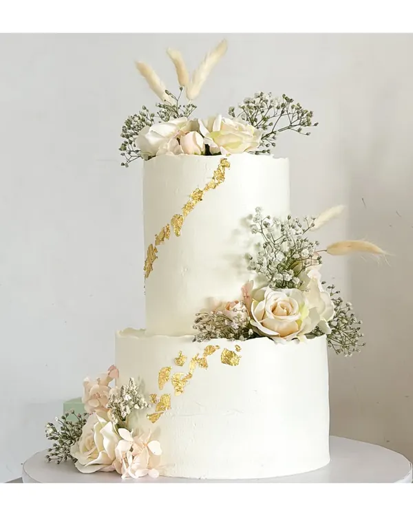 This timeless two-tier cake, adorned with delicate florals and a touch of gold leaf, is the perfect centerpiece for an elegant engagement or wedding celebration. It’s crafted with love and is completely eggless and free of fondant.