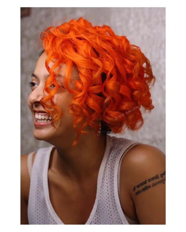 This vibrant orange on beautiful curls is what we call 'Summer is Here'. We used a high-impact neon orange to create a look that's as bright and energetic as our client.
