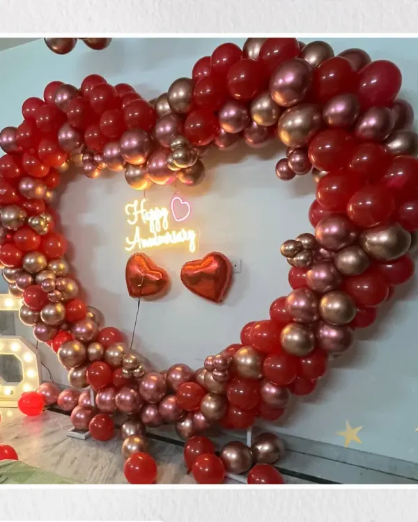 A grand gesture for a grand milestone. This 55th-anniversary celebration features a stunning heart-shaped arch made of red and chrome gold balloons, a "Happy Anniversary" neon sign, and a large marquee number to mark the special year.