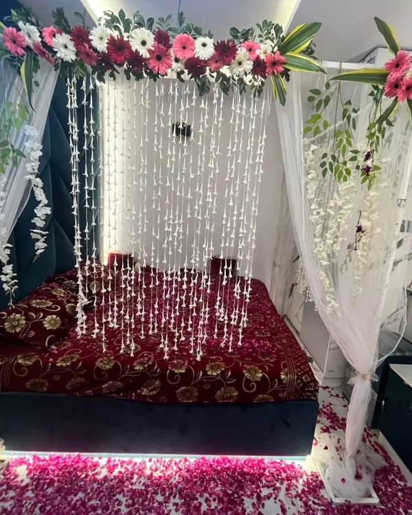 A stunning first night wedding decoration featuring a floral canopy with hanging jasmine strings over a bed covered in rose petals.