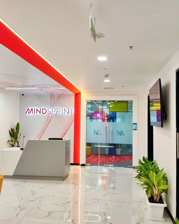 The main reception area for Mindsprint, featuring a clean, modern desk and prominent company branding. The red accent lighting and polished marble floors create a sleek and professional entry point for visitors.