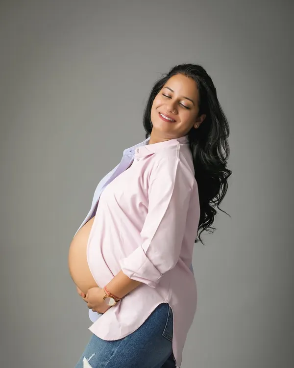 The pure joy and glow of motherhood. This mom-to-be looks so happy and relaxed in a casual open shirt and jeans, showing off her beautiful bump in a simple studio portrait.